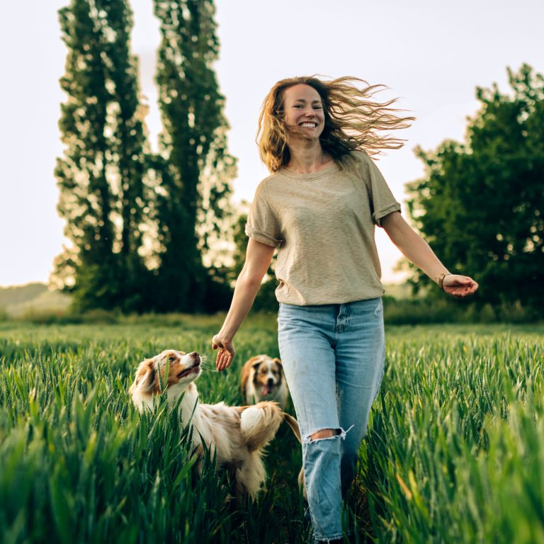 happy fulfilled woman running in a field with her dogs
