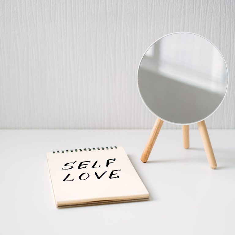 Self love, state of appreciation for oneself, physical, psychological and spiritual growth, taking care of own needs, wellbeing. Notepad with text Self love and reflection in the mirror.